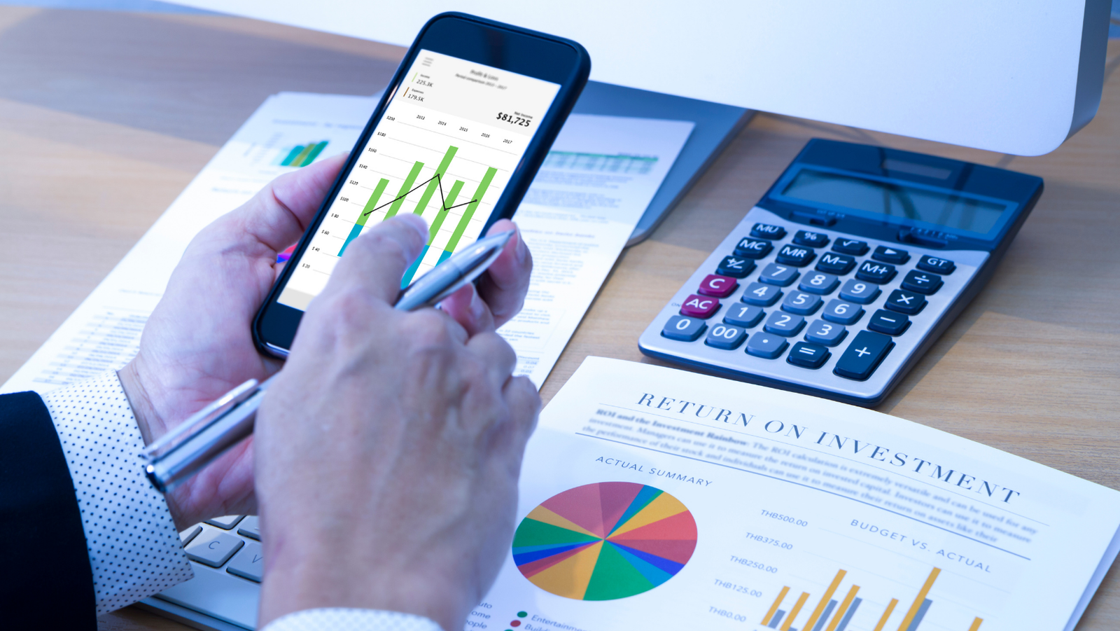 Person looking at phone with return on investment report on desk
